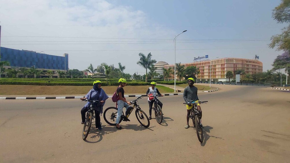 Four people on bicycles on a road with buildings in the background. 4