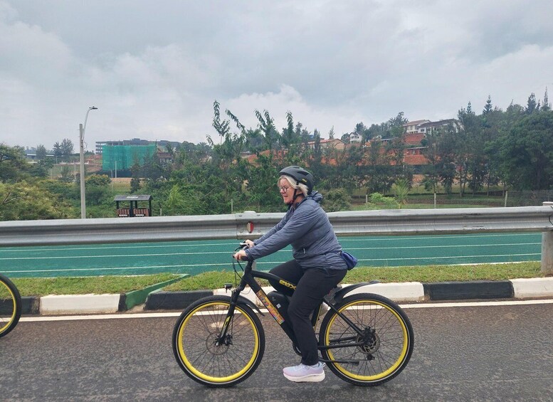 A person riding a bicycle on a paved path with a green running track in the background. 2