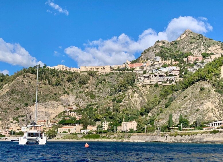 A coastal town with buildings on a hillside, a boat in the water, and a clear blue sky. 3