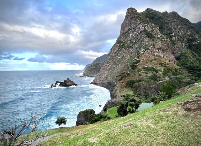 A coastal landscape with a prominent rocky cliff, ocean waves, and a grassy hillside. 1