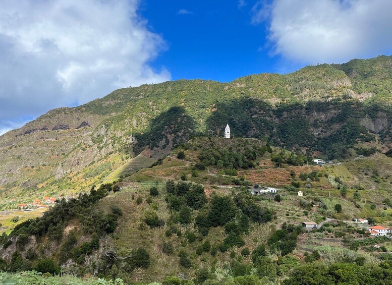 A mountainous landscape with terraced fields, a white church with a bell tower, and scattered houses. 2