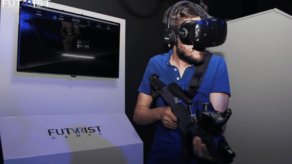 A person wearing a VR headset and holding a VR controller in front of a display labeled 'FUTVRIST GAMES.' 2