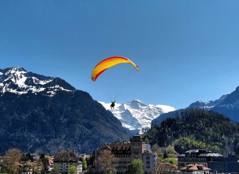 A paraglider over a mountainous landscape with snow-capped peaks and a town below. 5