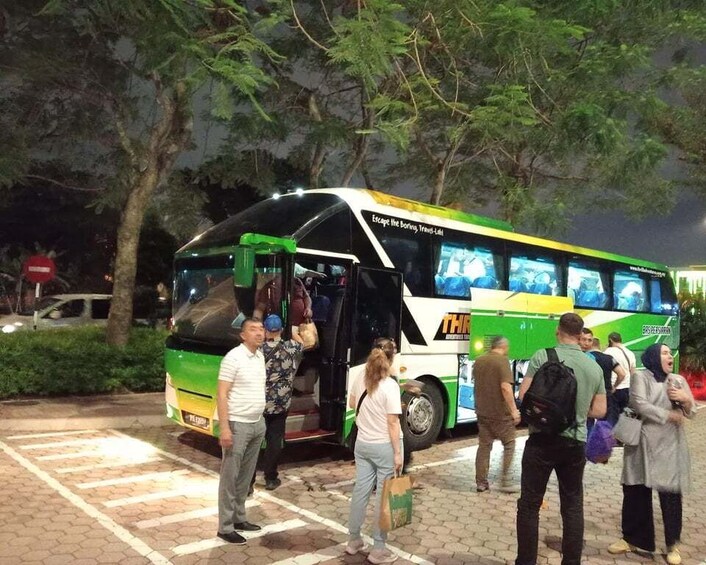 A nighttime outdoor scene with a green and white bus parked, people standing around, and trees in the background. 3