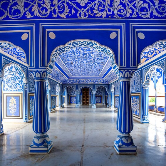 An ornate hall with blue and white patterns, large columns, and a central door. 5