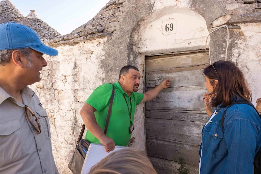 A man in a green shirt pointing at a door with the number 69. 3
