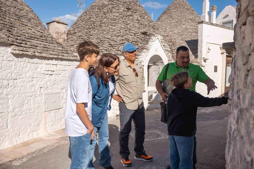 A group of people exploring a historical site with stone buildings and a white wall. 4