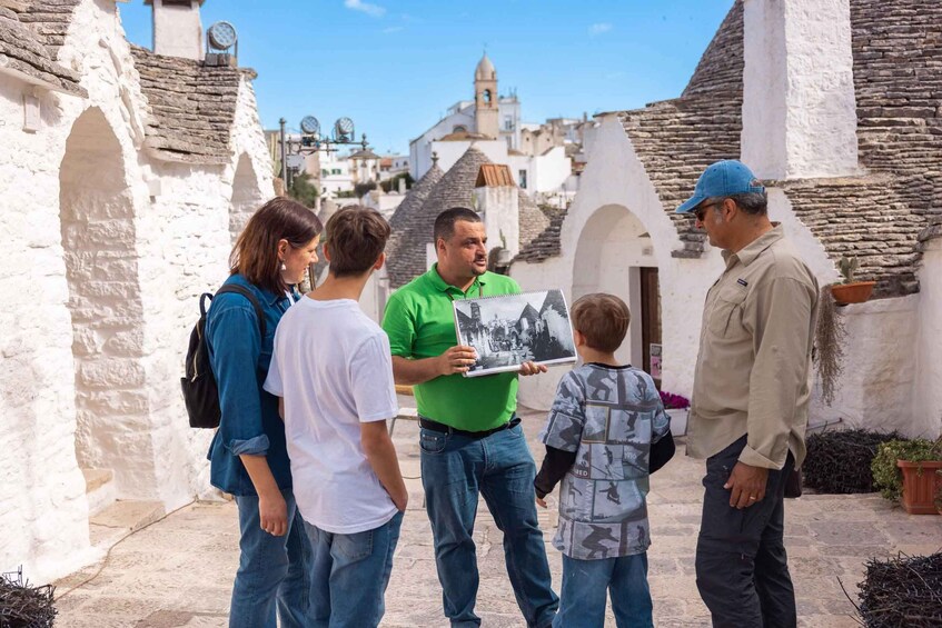 A group of people standing in a historical area with white stone buildings and a church in the background. 1