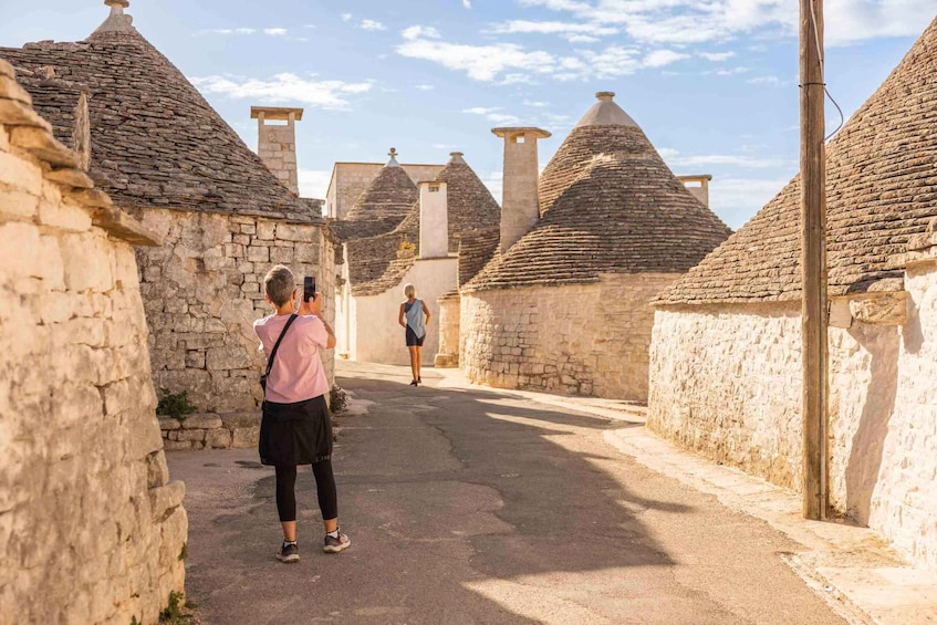 A narrow street lined with stone buildings with conical roofs. 5