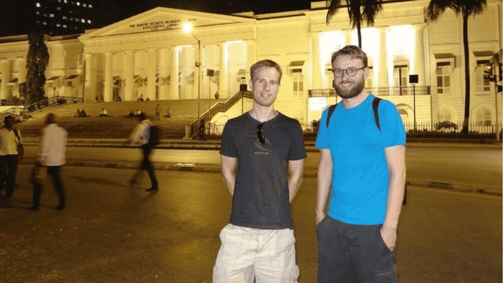 Two men standing in front of a large, illuminated building with columns and steps. 2