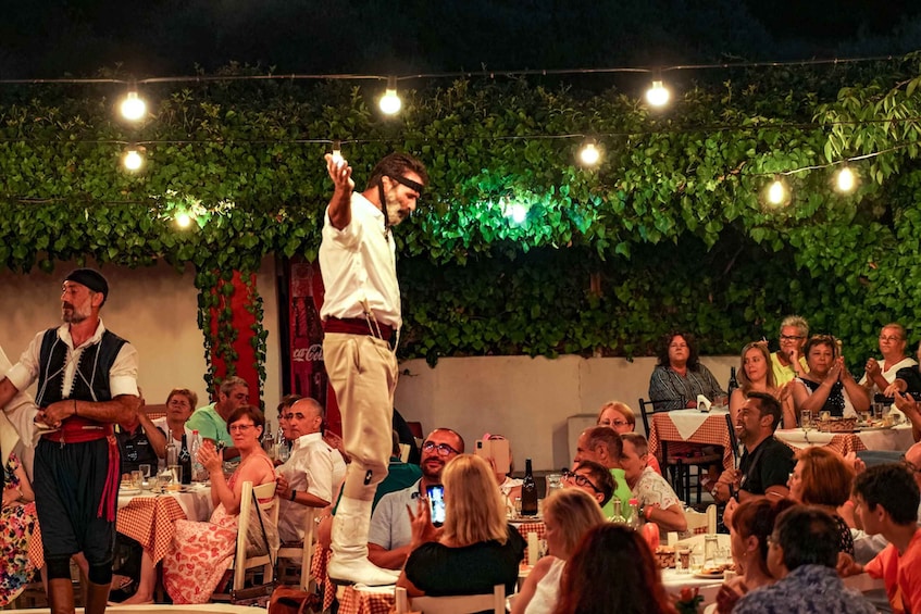 A man performing on a stage with a crowd seated at tables below. 1
