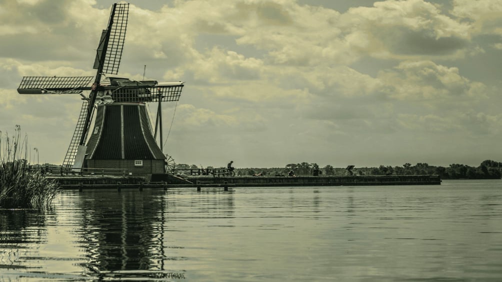A windmill by a calm river with a cloudy sky. 2