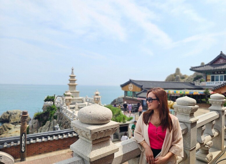 A person standing on a stone balustrade overlooking a traditional pagoda and a body of water. 3