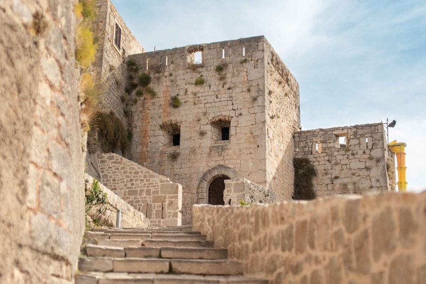 Un escalier en pierre mène à une structure imposante, semblable à une forteresse, dotée d’ouvertures en arc et surplombée par un ciel dégagé. 2
