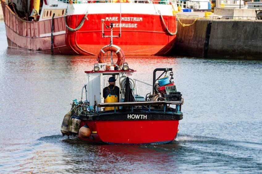 A red boat named 'HOWTH' with a person on board, docked near a larger red ship. 5