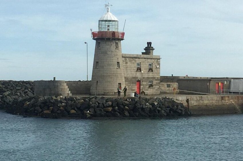 A lighthouse with a red top, a stone building, and a rocky breakwater. 2