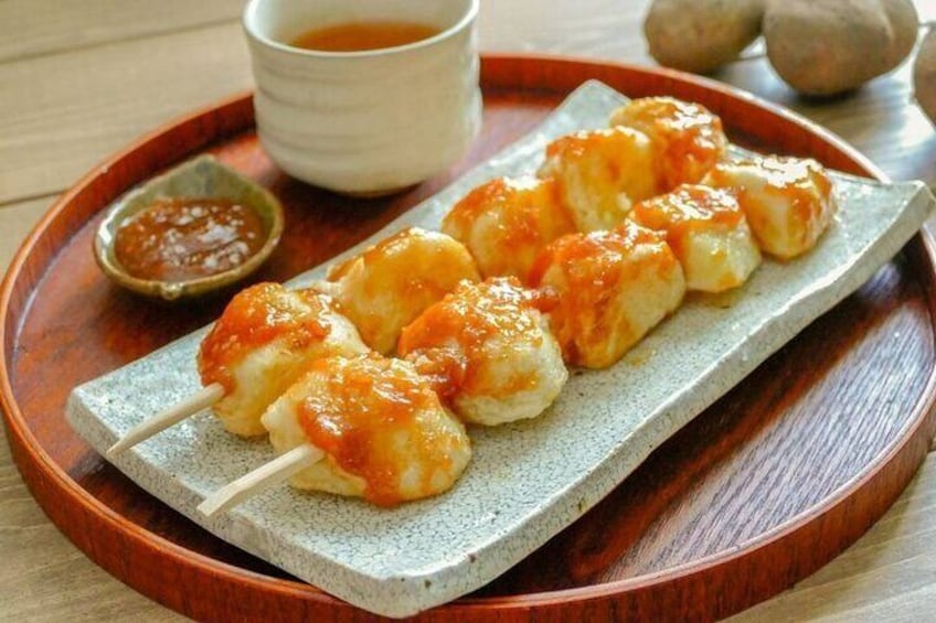 Skewers of grilled chicken with a glaze, served on a ceramic plate with a dipping sauce. 2