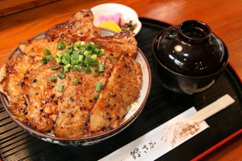 A plate of grilled fish garnished with green onions, accompanied by a small bowl of sauce and a dark ceramic container on a black tray. 3