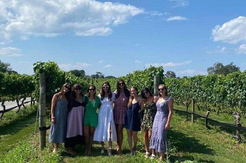 A group of people standing in a vineyard with rows of grapevines in the background. 2