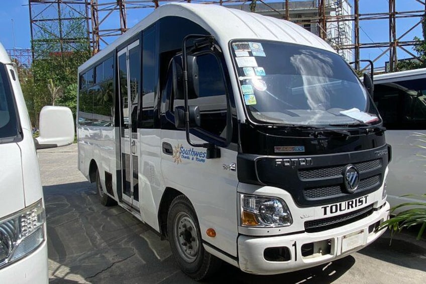 A white tour bus with the word 'TOURIST' on the front, parked in a lot with other vehicles and a building with scaffolding in the background. 5