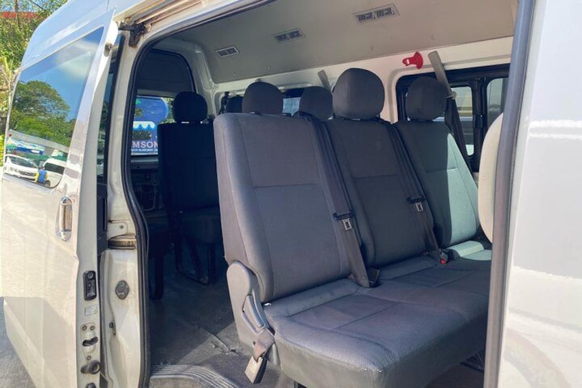 The interior of a white van with two rows of seats, a visible door handle, and a rearview mirror. 2