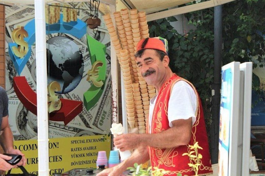 A man in a red vest standing at a booth with a globe and currency symbols in the background. 3