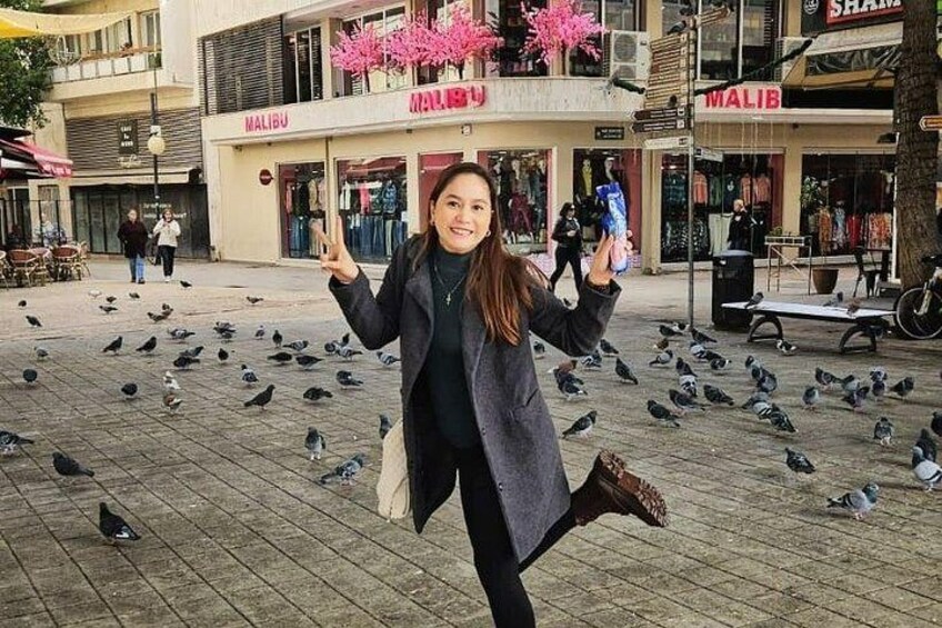 Una persona con abrigo largo, con palomas en el suelo, en un entorno urbano con escaparates. 5