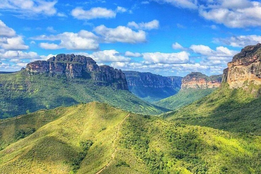 A mountainous landscape with green valleys and rocky cliffs under a blue sky with clouds. 4
