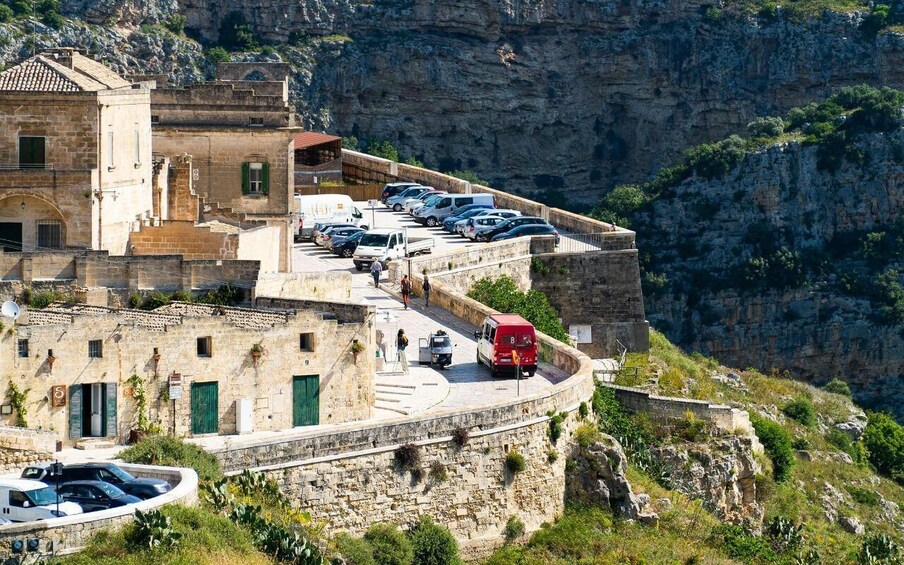 A coastal town with stone buildings, a curved road, parked cars, and cliffs. 1