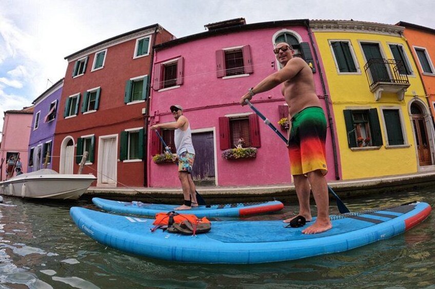 Dos personas en un bote inflable azul en un canal, con edificios coloridos al fondo. 1