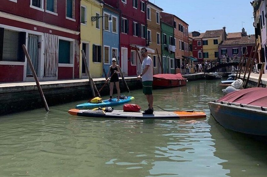 Un canal con edificios de colores, una persona de pie en una tabla de remo y otra en kayak. 2
