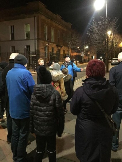 A group of people gathered on a city street at night, with buildings and streetlights in the background. 2