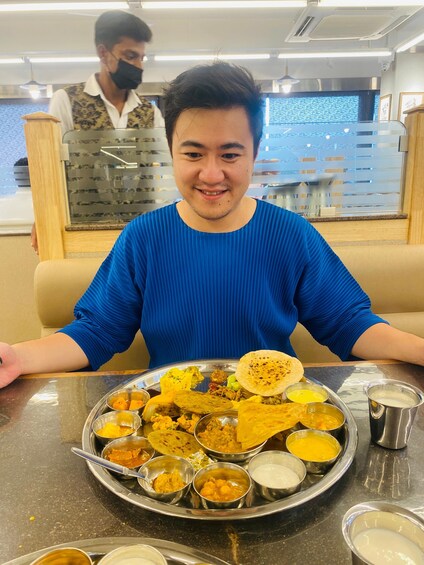 A person seated at a table with a variety of Indian dishes. 3