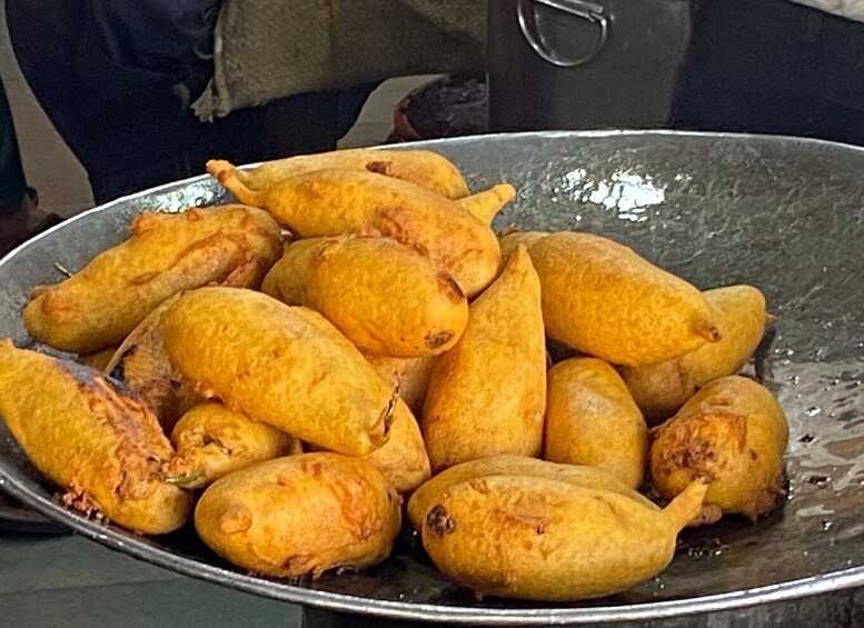 A large metal bowl filled with golden-brown fried items, likely a type of traditional snack or street food. 4