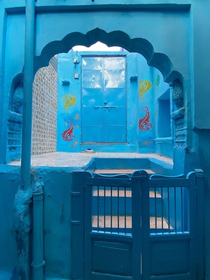 A blue-walled building with a central door, decorative arches, and colorful wall paintings. 1