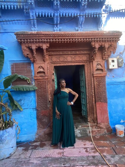 A woman in a green dress standing in front of a blue building with intricate carvings. 5