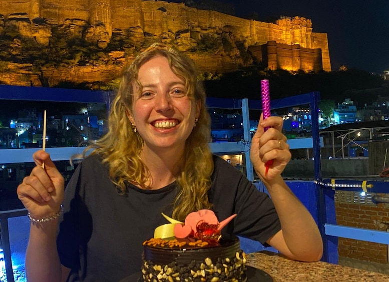A person holding a toothpick and a pink object, with a cake in front of them. 1