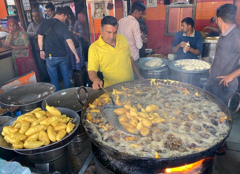 A street food vendor cooking at a large outdoor grill with several people around. 4