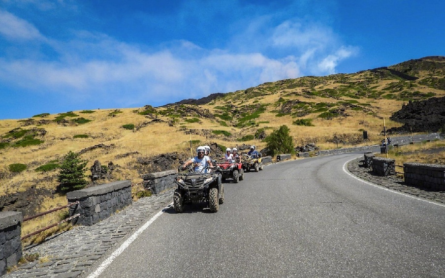 A group of people riding ATVs on a winding road surrounded by hills. 1
