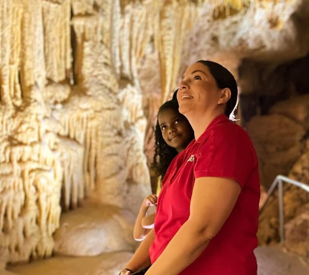 A person in a red shirt standing in front of a cave with stalactites. 1