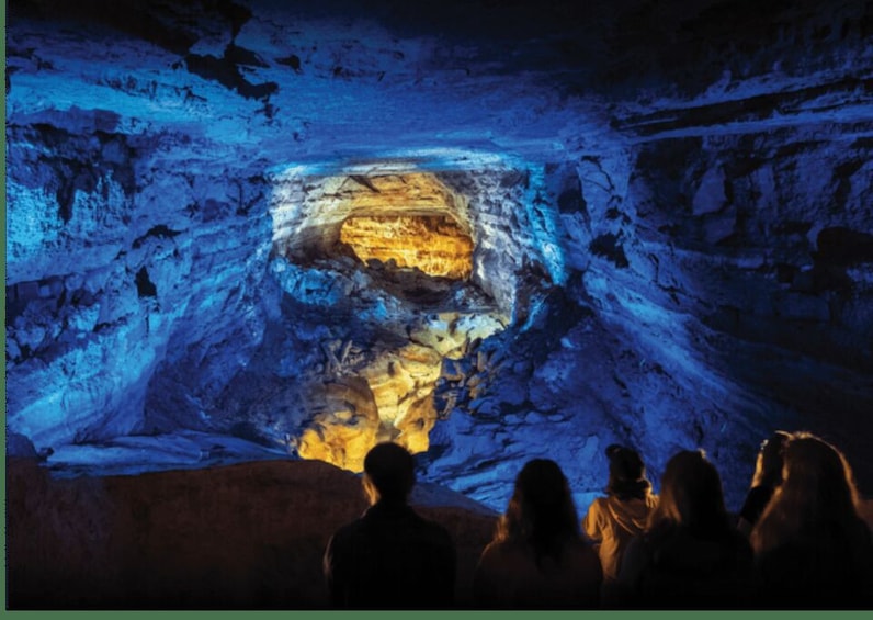 A group of people observing a cave with illuminated rock formations. 2