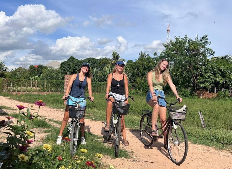 Three people riding bicycles on a dirt path surrounded by greenery and flowers. 1