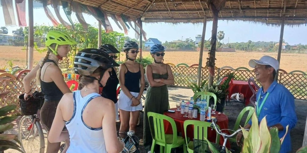 A group of cyclists at a covered outdoor area with a table set for refreshment. 5