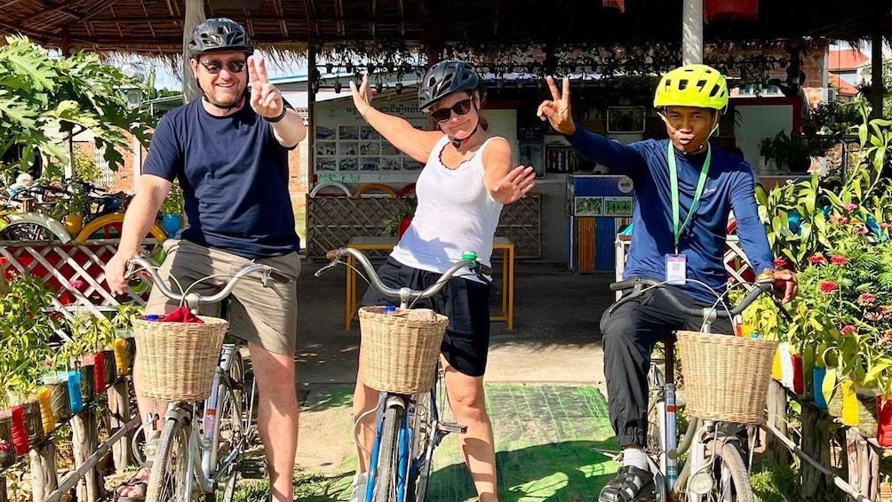 Three people on bicycles with baskets, a covered structure, and a fence with colorful decorations. 3