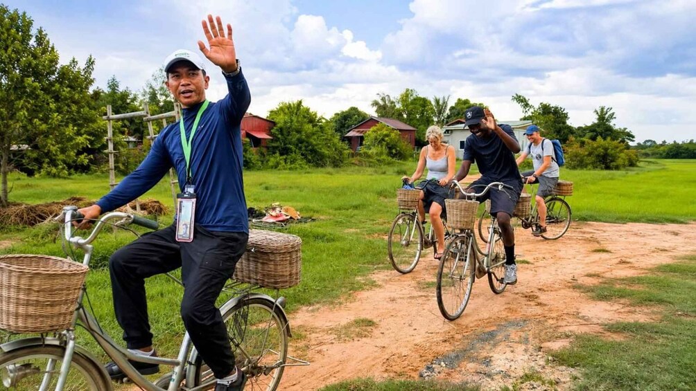 A person on a bicycle with a basket, another on a bicycle with a basket, and two others on bicycles in a rural setting. 1