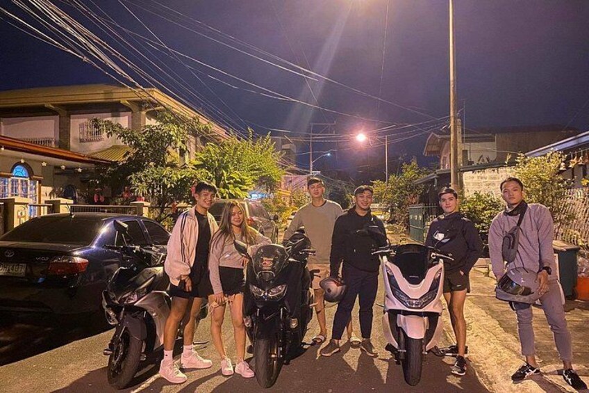 A group of people standing on a street at night with motorcycles and a car parked nearby. 3