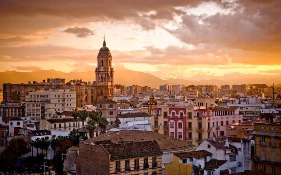 A cityscape with a prominent church tower, dense urban buildings, and a sunset sky. 3