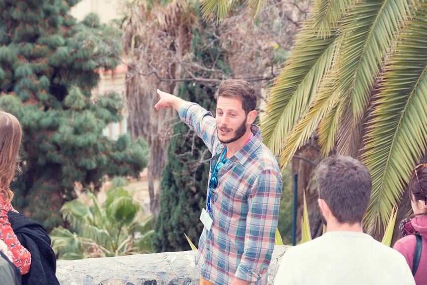 A man in a plaid shirt pointing at something, surrounded by people and palm trees. 2