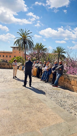 A group of people gathered around a guide, standing on a cobblestone path with palm trees and flowering shrubs in the background. 4