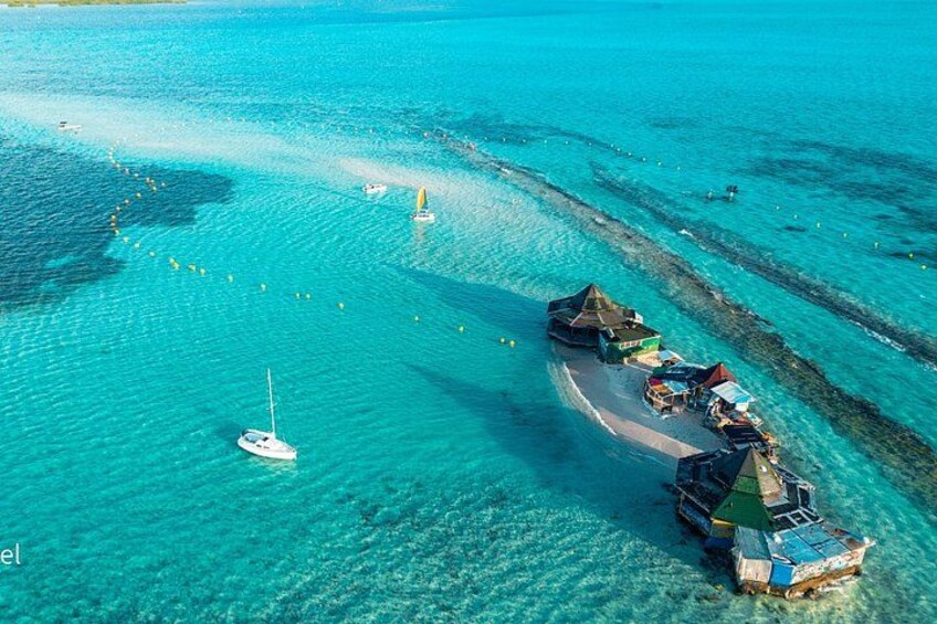 A turquoise sea with a boat and a small island with huts. 1